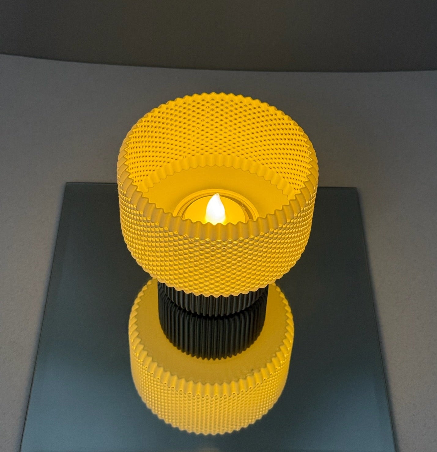Yellow textured candle holder with a lit candle on a reflective surface