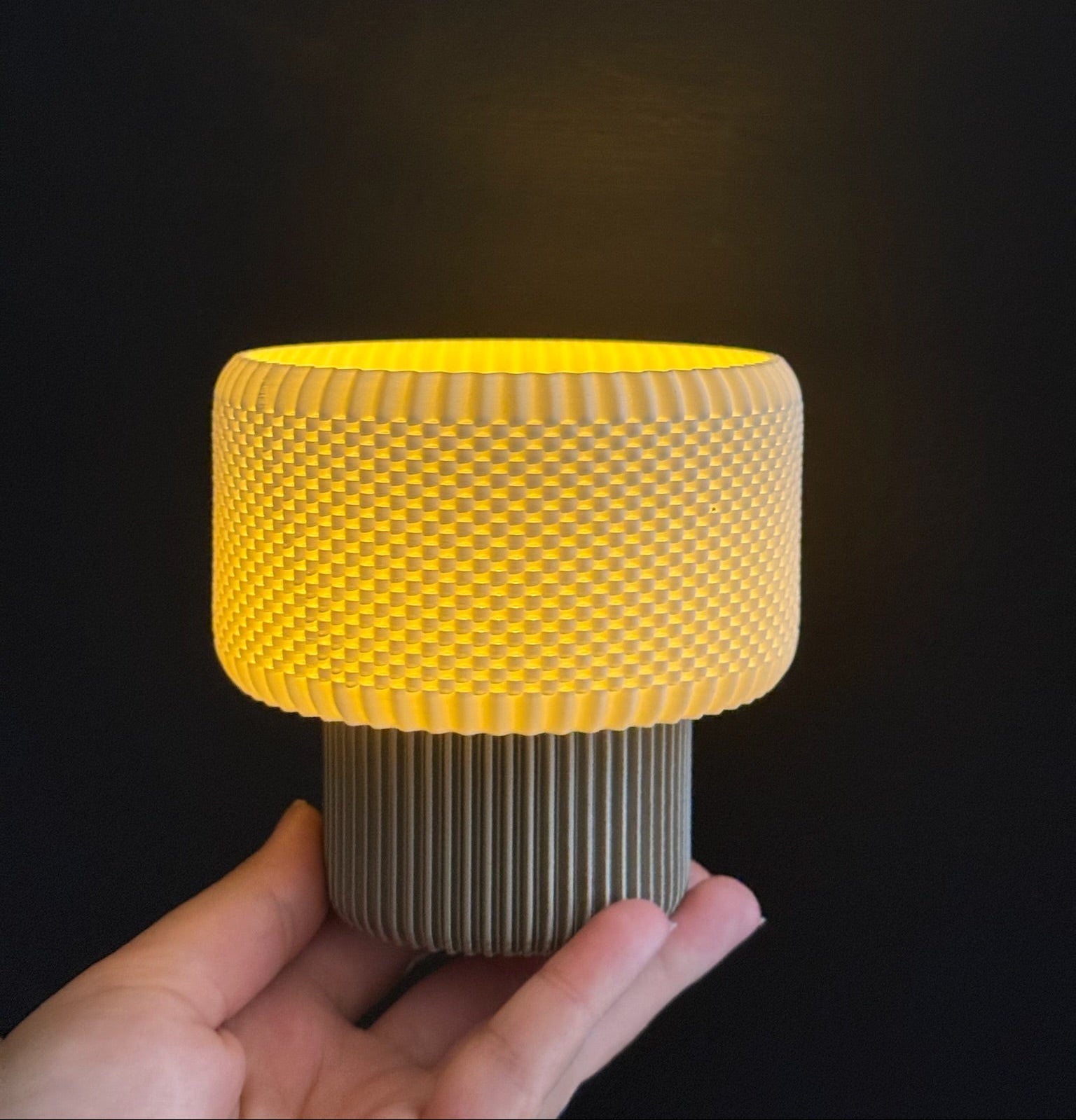 Hand holding a cylindrical object with a yellow top and textured gray base against a dark background