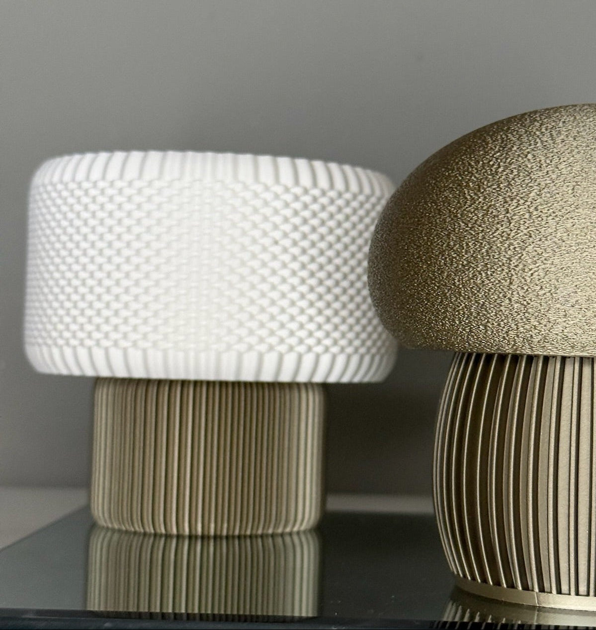 Two textured stools, one white and one gold, on a reflective surface with a neutral background.